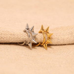 May include: Two hoop earrings, one silver-toned and one gold-toned, each featuring a row of four sharp, conical spikes extending outward from the outer edge of the circular band. The metallic finish is smooth and reflective on both pieces.