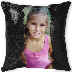 May include: Square pillow with a reversible sequin design. One side features a smiling girl in a pink tank top, the other side is black. The sequins can be flipped to reveal the image or the solid black color.