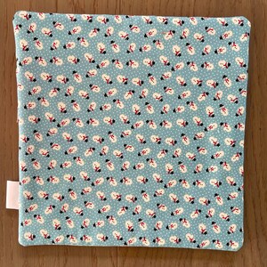 May include: A square, light blue fabric with a repeating pattern of snowmen wearing black top hats and red scarves. The snowmen are set against a background of white dots. A white tag is attached to the side of the fabric.