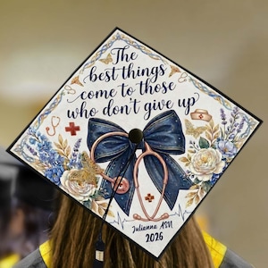 May include: A decorated graduation cap with a navy bow, stethoscope, and floral design. The cap displays the text "The best things come to those who don't give up" and the name "Julianna ASN 2026".