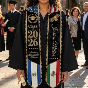 May include: A smiling graduate in a black cap and gown, wearing a sash with the text "Class of 2026" and "University of Southern California." The sash features the American and Mexican flags. She holds a rolled diploma.