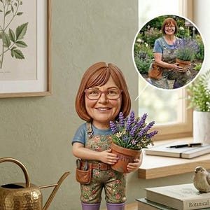 May include: A custom bobblehead figurine of a person with shoulder-length brown hair and glasses, wearing a floral print overall, blue shirt, and purple boots. The figure holds a terracotta pot of lavender and stands on a base labelled Oasis's Garden.