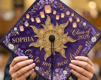 May include: A purple graduation cap with gold accents, featuring a sun design and the name "Sophia." The cap is decorated with floral elements, lanterns, and the text "Class of 2026" and "On to my new dream."
