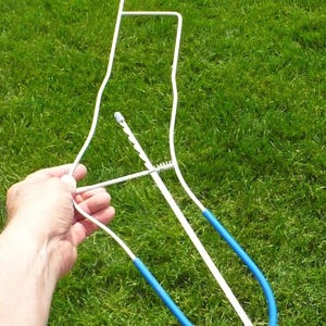 May include: A white metal clothes hanger with a blue rubber coating on the bottom section. The hanger has a hook at the top and a spring mechanism. The item is designed for hanging clothes.