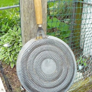 May include: A vintage metal stovetop burner diffuser with a wooden handle. The diffuser has a circular design with multiple holes.