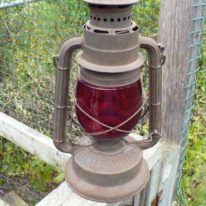 May include: A vintage rusty metal lantern with a red glass globe and the words "Little Wizard" on the base.