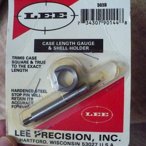 May include: A red and white package for a Lee Precision case length gauge and shell holder for 303B caliber. The package includes a hardened steel stop pin and a gauge with a ring. The text on the package reads "Lee Precision, Inc. Hartford, Wisconsin 53027 U.S.A."