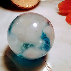 May include: A clear glass sphere with blue and white swirls inside. The sphere is sitting on a white surface.