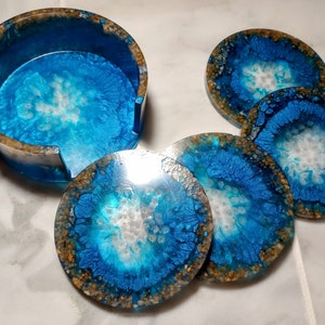 May include: Set of six blue and white resin coasters with a glittery finish. The coasters have a unique, abstract design with a white center and blue edges. The coasters are perfect for protecting your furniture from scratches and spills.