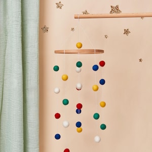 May include: A wooden baby mobile with colourful felt balls hanging from a circular wooden frame. The balls are red, yellow, green, blue and white.