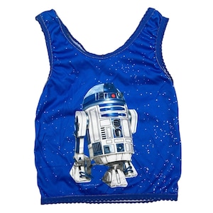 May include: A blue tank top with a white and gray R2-D2 graphic on the front. The tank top has a white star pattern on a blue background.