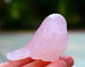 May include: A pink rose quartz bird carving. The bird is detailed with feathers and has a smooth, polished finish.