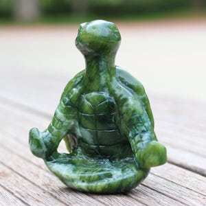 May include: Green jade turtle sculpture in a meditating pose. The turtle has a detailed shell and is carved with a serene expression.