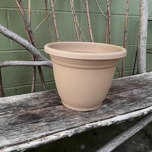 May include: A brown plastic planter pot with a smooth, rounded surface. The pot is sitting on a weathered wooden bench.