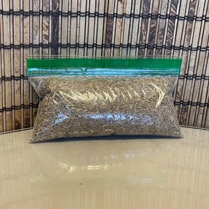 May include: A clear plastic bag with a green zipper closure filled with brown grass seed.