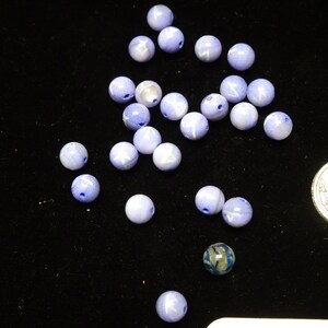 May include: A collection of light blue and white agate beads with a mottled pattern. The beads are scattered on a black surface.