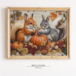 May include: A framed embroidery art piece featuring a ginger squirrel and a grey squirrel sitting beside a large orange pumpkin. The scene is decorated with autumn leaves, smaller pumpkins, and nuts on a light fabric background. Text reads BELLA FLORA Studios.