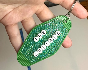 Llavero artesanal con diseño de rivalidad acalorada y adornos brillantes.
