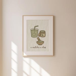 May include: A framed print featuring matcha-themed illustrations. The artwork includes a matcha drink with ice, a jar, and a bowl with a whisk. The text "a matcha a day" is written at the bottom. The background has vertical stripes.