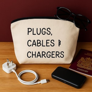 May include: A cream-coloured travel pouch with the words "PLUGS, CABLES & CHARGERS" printed in black. The pouch is next to a white plug, a white cable, a black portable charger, a pair of sunglasses, and a passport.