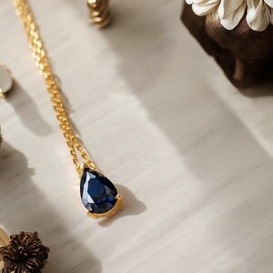 Peut inclure: Un collier en chaîne dorée avec un pendentif en forme de larme orné d'une pierre précieuse bleu foncé.