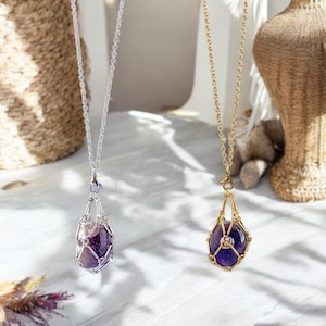 May include: Two necklaces with amethyst stones encased in a cage-like pendant. One necklace has a silver chain and pendant, the other has a gold chain and pendant.