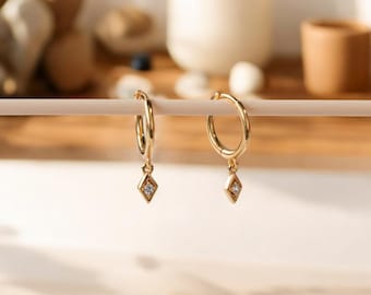 May include: A pair of gold hoop earrings with a small diamond-shaped pendant hanging from each hoop.
