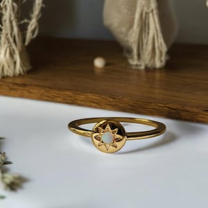 May include: A gold ring featuring a round opal stone set within a starburst design.