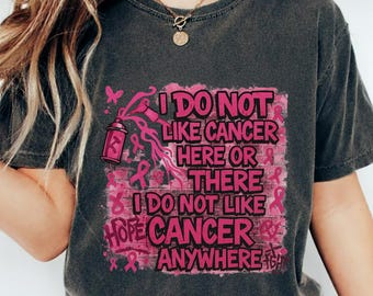May include: Dark gray t-shirt with a pink graphic that reads "I DO NOT LIKE CANCER HERE OR THERE I DO NOT LIKE CANCER ANYWHERE." The design includes a spray can, ribbons, and butterflies.