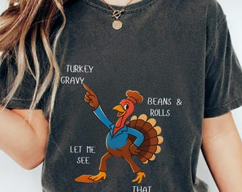 Puede incluir: Camiseta gris oscuro con un pavo de dibujos animados con un gorro de chef, que señala el texto "Turkey Gravy", "Beans & Rolls" y "That Casserole". La camiseta también tiene el texto "Let Me See". La palabra "Pepper" está en un rectángulo verde.
