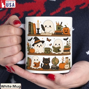 May include: A white ceramic mug featuring a three-tiered shelf illustration. The design includes cartoon ghosts, a black cat, pumpkins, books, a candle, a globe, a camera, and a mug labeled BOO-RS. The art style is colorful and detailed.
