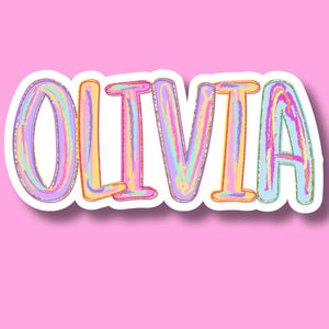 May include: A sticker featuring the name OLIVIA in bold, uppercase letters. The text has a multi-colored, marbled effect with shades of purple, pink, yellow, and blue, outlined in a thin gold border and a thick white edge against a pink background.