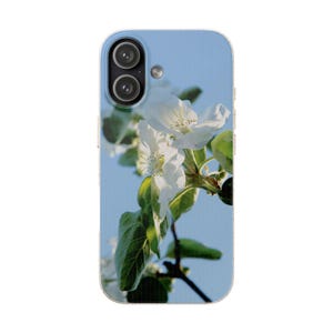 Könnte beinhalten: Eine rechteckige Smartphone-Hülle mit hellblauem Hintergrund, bedruckt mit einem Foto von weißen Apfelblüten an einem Zweig mit grünen Blättern. Die Hülle hat oben links eine Aussparung für eine Doppelkamera mit schwarzen Rändern.