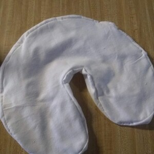 May include: White fabric u-shaped pillow for neck support.