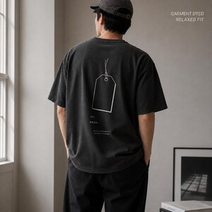 May include: A charcoal grey short-sleeve t-shirt with a relaxed fit and garment-dyed finish. The back features a white line-art graphic of a gift tag with the text TO: and FROM: printed below, along with the words QUIET INTENSITY OBJECT STUDIES.