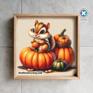 May include: A pixel art illustration of a brown and white chipmunk sitting on a large orange pumpkin, next to a smaller orange pumpkin and a dark green pumpkin. The text BeeStitchU.Etsy.com is printed in black at the bottom of the framed artwork.