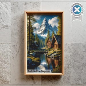 May include: A framed cross-stitch pattern depicting a mountain landscape with snow-capped peaks, evergreen trees, and wooden cabins situated along a river. The text BeeStitchUa.Etsy.com is printed at the bottom, and a TESTED badge is in the corner.