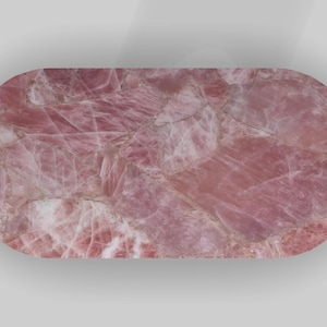 May include: A pink rose quartz slab with an oval shape. The surface displays a natural pattern of varying shades of pink and white, creating a marbled effect. The stone is polished and smooth, with a subtle sheen.