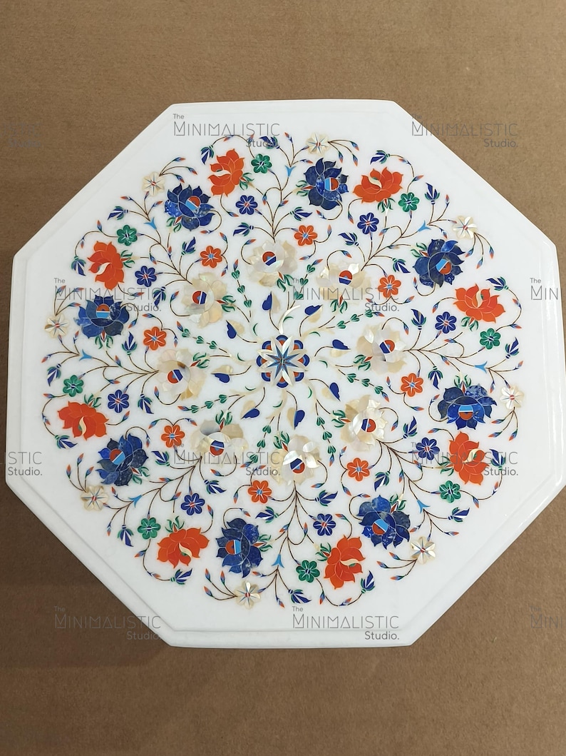 May include: White octagonal marble table with floral inlay. The design features orange, blue, and white flowers with green leaves. The table has a polished finish and is suitable for indoor use.