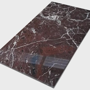 May include: A rectangular, polished marble slab with a deep burgundy base color and intricate white veining patterns. The surface reflects light, highlighting the natural stone's texture and design. The slab is ideal for countertops or decorative surfaces.