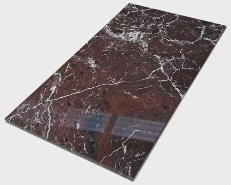May include: A rectangular, polished marble slab with a deep burgundy base color and intricate white veining patterns. The surface reflects light, highlighting the natural stone's texture and design. The slab is ideal for countertops or decorative surfaces.