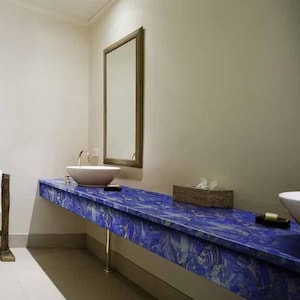 Può includere: Un moderno mobile da bagno con un vivace piano blu con un motivo unico. Il mobile ha un lavandino bianco, un rubinetto dorato e uno specchio rettangolare. Sono visibili anche un cestino intrecciato e un portasapone.