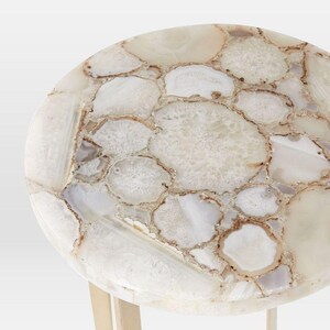 May include: A round side table with a top made of white and cream-colored agate stone slices. The agate pieces are outlined with brown and tan hues. The table has a light-colored, possibly gold, metal base.