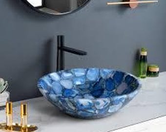 Könnte beinhalten: Ein blau-weißes Waschbecken mit Mosaikmuster. Das Waschbecken ist rund und steht auf einer weißen Arbeitsplatte. Ein schwarzer Wasserhahn ist hinter dem Waschbecken montiert. Dekorative Gegenstände sind im Hintergrund.