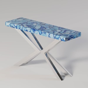 May include: A rectangular console table with a blue and white stone top and a polished silver metal X-shaped base. The tabletop features a mosaic pattern of blue and white stones. The table is approximately 48 inches long.