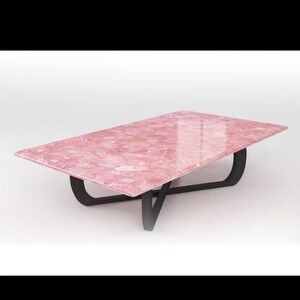 May include: A rectangular coffee table with a pink, patterned top and a black metal base. The table's top has a glossy finish and the base has a modern, geometric design. The table is approximately 122 cm long and 61 cm wide.