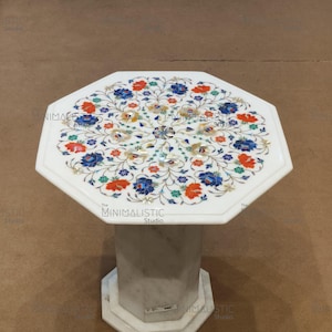 May include: White marble side table with an octagonal top and base. The tabletop features a floral inlay design with blue, orange, and green accents. The table is supported by a geometric pedestal.