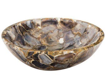 May include: A decorative, oval-shaped bowl with a mosaic design. The bowl is made of polished, natural stone in shades of brown, gray, and cream. The bowl's interior is smooth and reflective, and the exterior has a textured appearance.