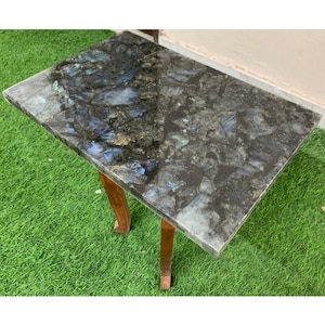 May include: A rectangular side table with a polished, dark gray tabletop inlaid with blue and gray stone. The table has four wooden legs. The tabletop measures approximately 30 inches long and 20 inches wide.