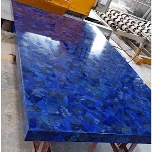 Könnte beinhalten: Eine große, rechteckige Arbeitsplatte mit einer mosaikartigen Oberfläche in tiefen Blau- und Indigotönen. Der polierte Stein reflektiert das Licht und erzeugt ein glänzendes Aussehen. Die Arbeitsplatte besteht wahrscheinlich aus Naturstein.